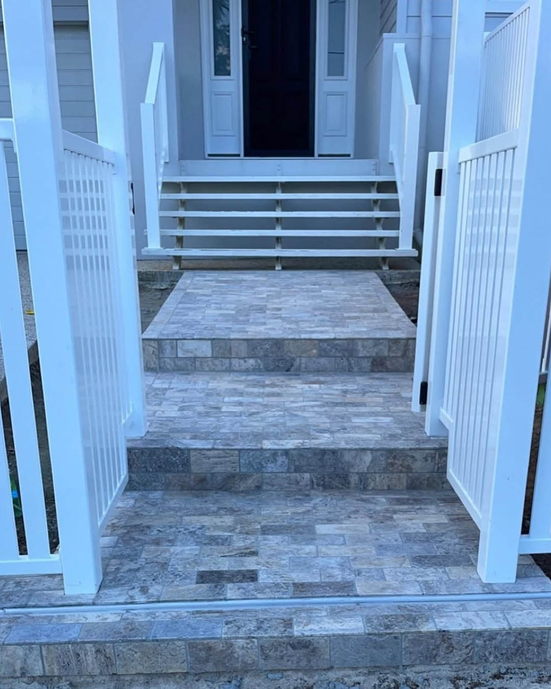 Grey stone-tiled front steps and path between open white gates