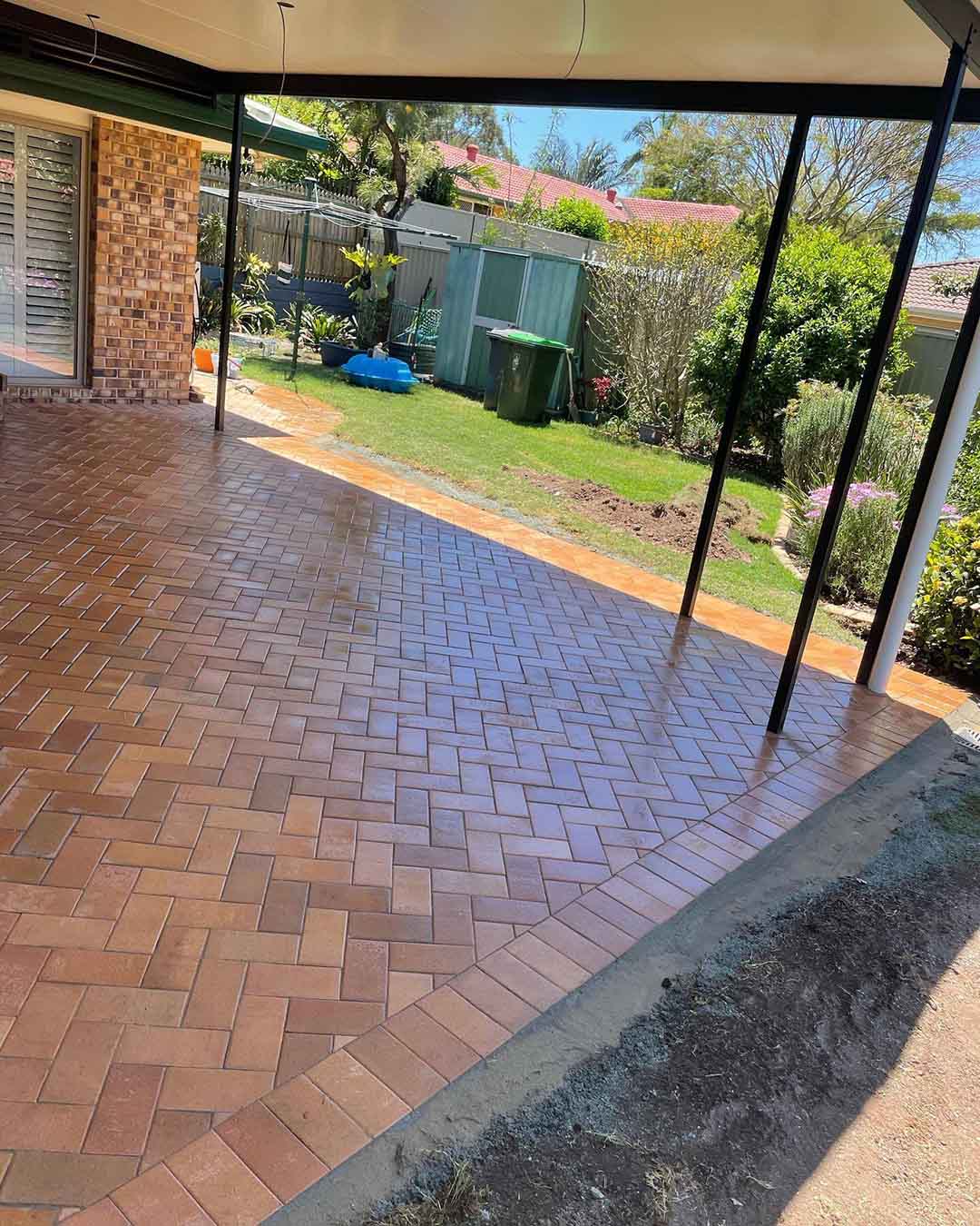 Red herringbone brick pavers under a covered patio beside a lawn