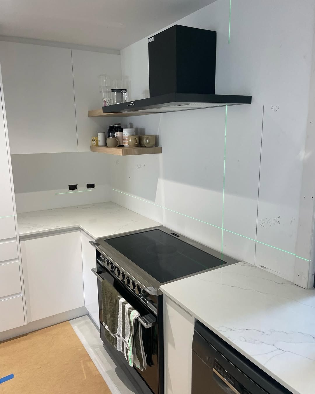 White kitchen with black rangehood and green laser level lines on the bare wall