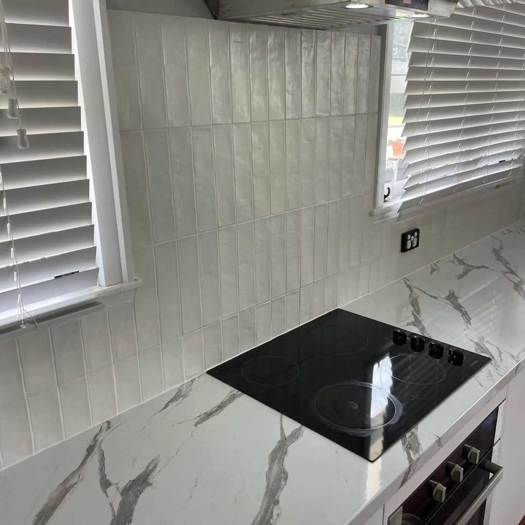 White vertical splashback tiles behind a black cooktop and marble-look benchtop
