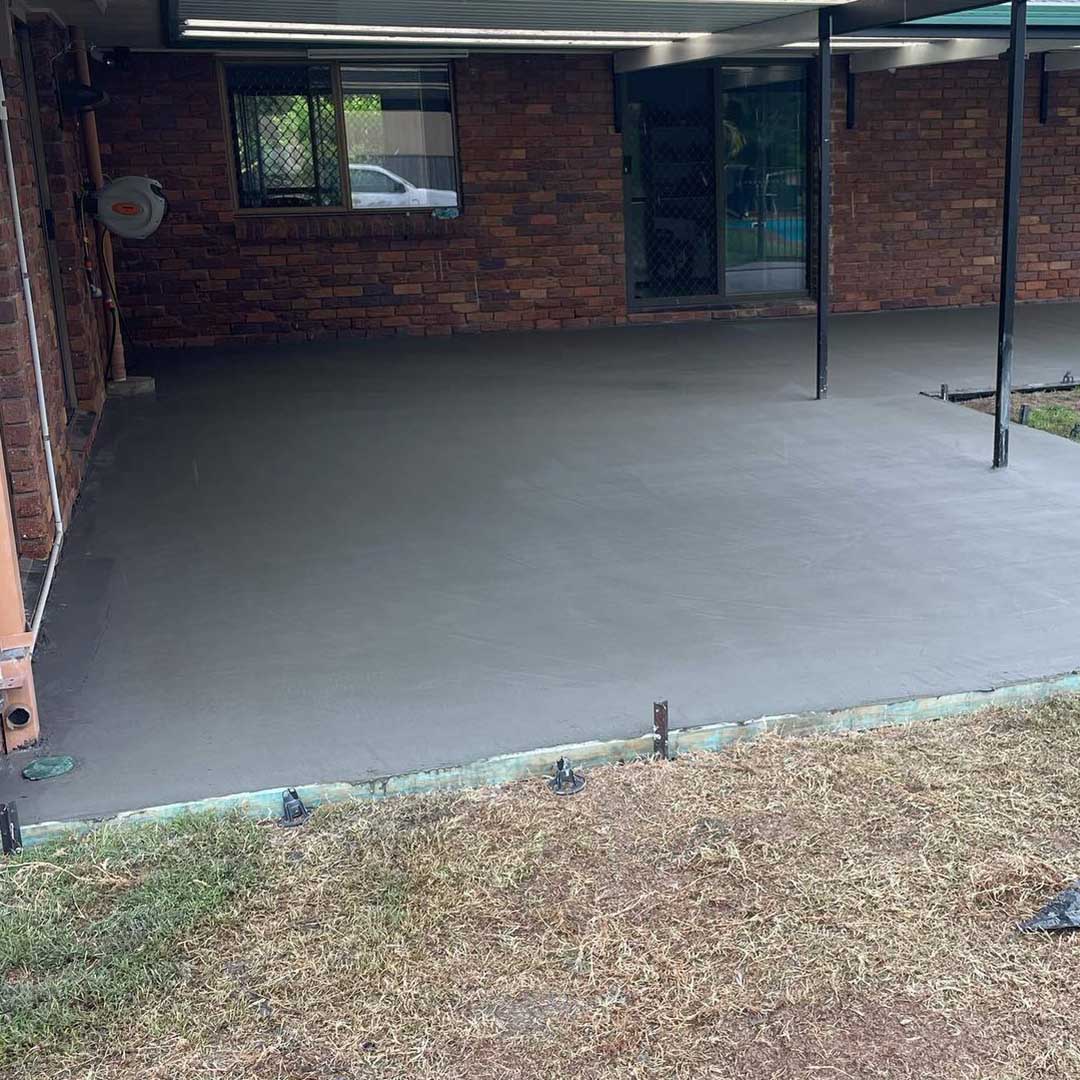 Fresh concrete slab under a patio roof beside a brick house