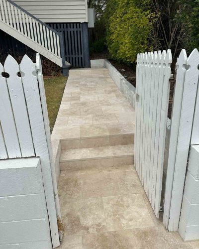 Pale stone pavers and steps through a white picket gate