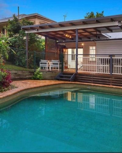 Pool with brick coping in front of a raised timber deck and pergola