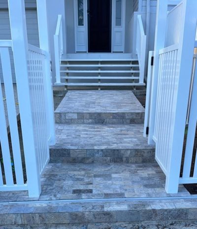 Stone-tiled front steps leading up to a house entry between white gates