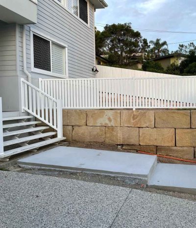 New concrete landing at the base of white stairs beside a sandstone block wall