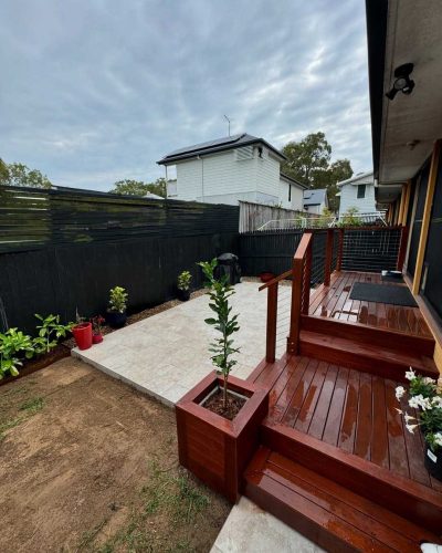 Timber deck and steps beside a pale paved path along a black fence