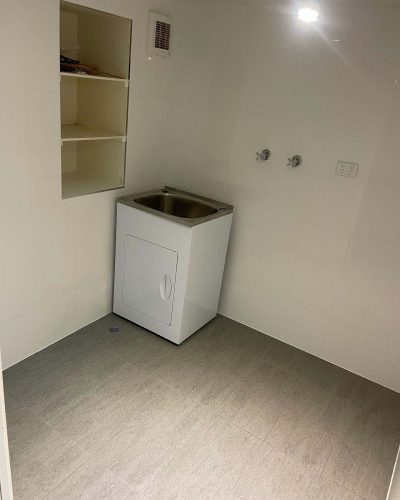 Tiled laundry with white walls, grey floor, laundry tub and open shelves