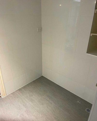 Empty laundry corner with white wall tiles and grey floor tiles