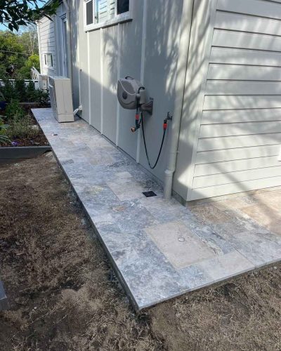 Grey stone pavers along a house wall with a hose reel, wider view