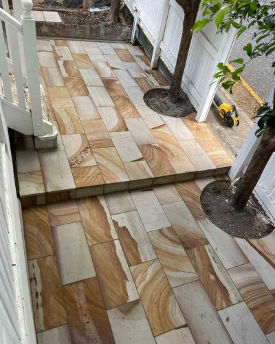 Sandstone-coloured pavers with a step down, laid around two trees