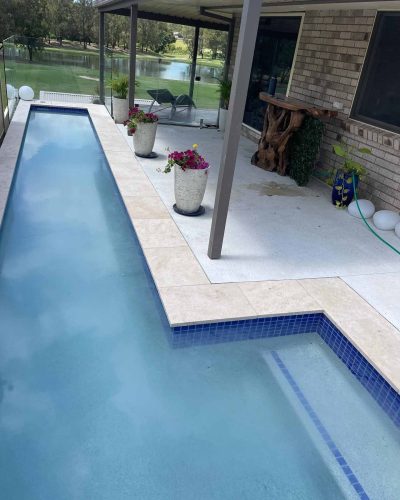 Lap pool with blue tile edging beside pale pavers and potted plants