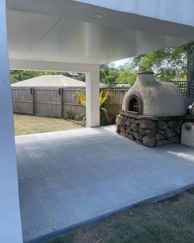 Concrete slab under a covered area beside a stone pizza oven