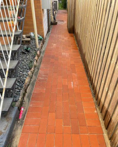 Red brick paved side path between outdoor stairs and a timber fence