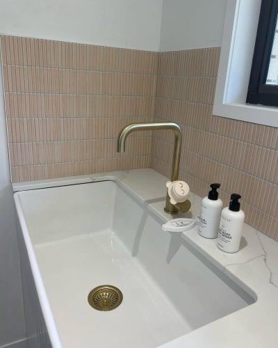 Pink vertical finger-tile splashback behind a white sink with a brass tap