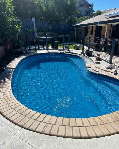 Kidney-shaped pool with brick coping in a fenced backyard with a patio