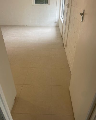 Empty room with large beige floor tiles, seen from the doorway
