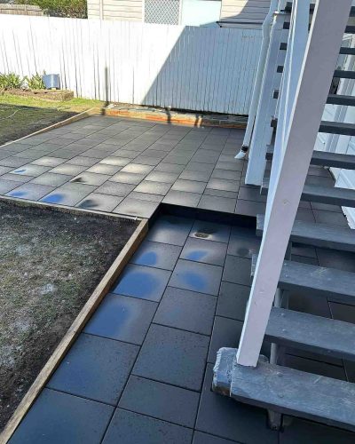 Dark grey square pavers laid around the foot of white outdoor stairs