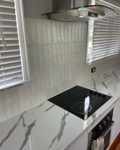 White gloss splashback tiles beside a window above a black cooktop
