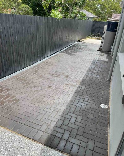 Long herringbone paved side path between a house and a dark fence