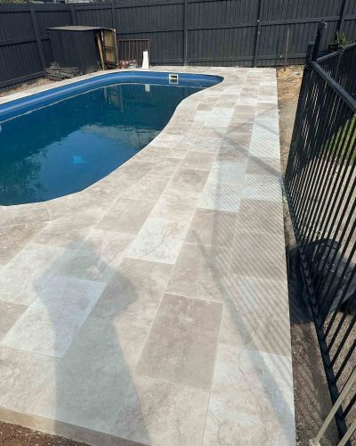 Pale stone pavers along a pool beside a black pool fence